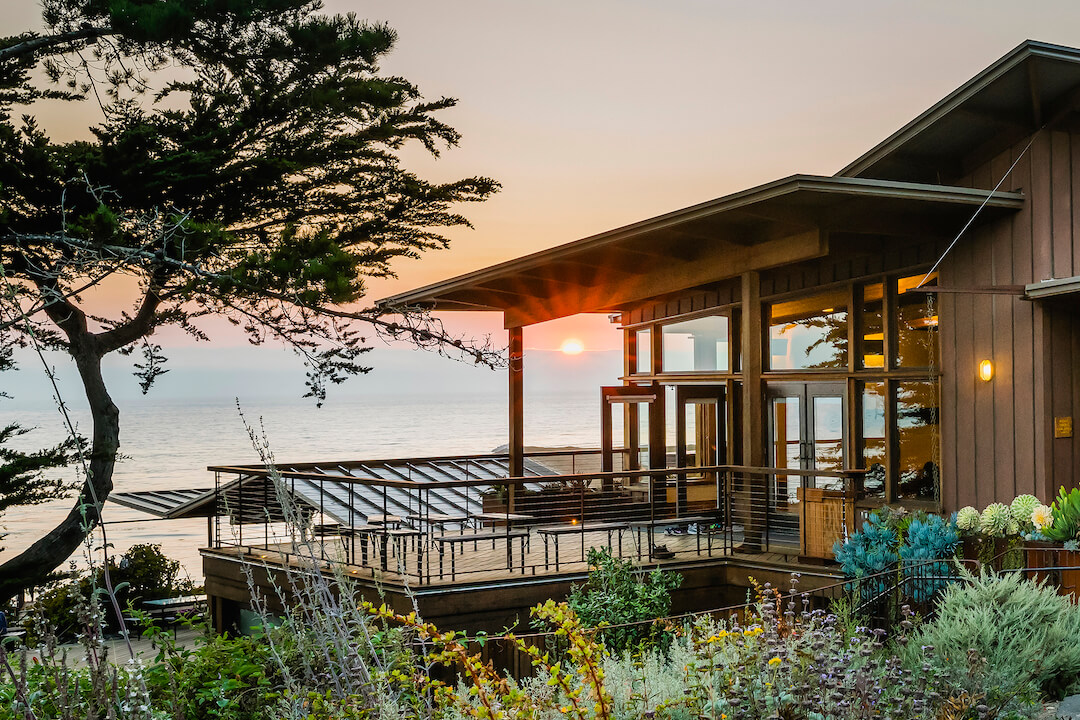 Sunset over the ocean with deck and buildings of wellness retreat in the foreground at one of the best wellness retreats in the US.